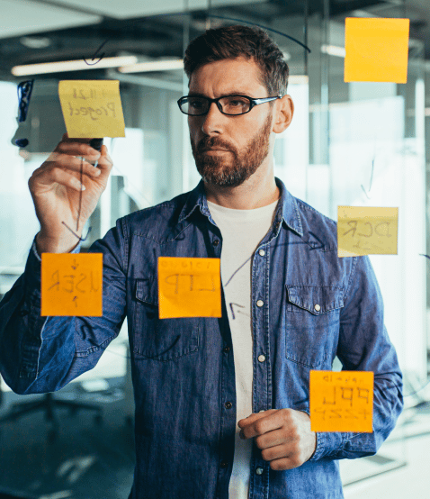 Man wearing glasses writes on sticky notes stuck to a glass wall