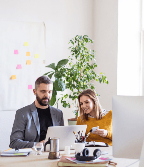 Man and women sit looking at a laptop together in an office space