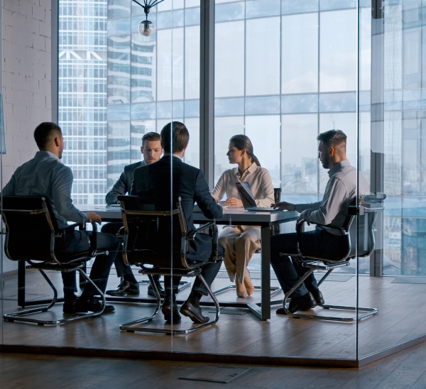 A team of 5 meet around a table in a glass office with large windows