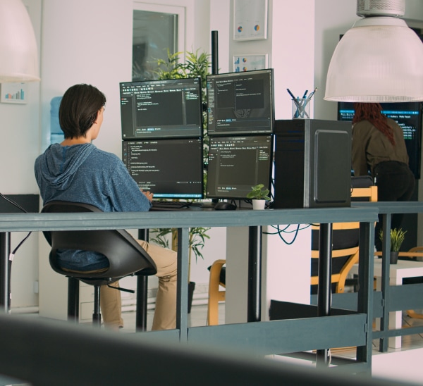 Man sits at multiple computer monitors and codes